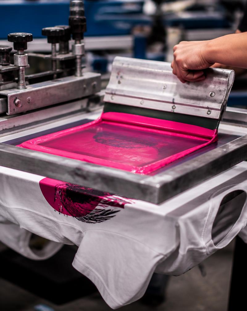 Screen printing press in action with vibrant pink ink on a white t-shirt